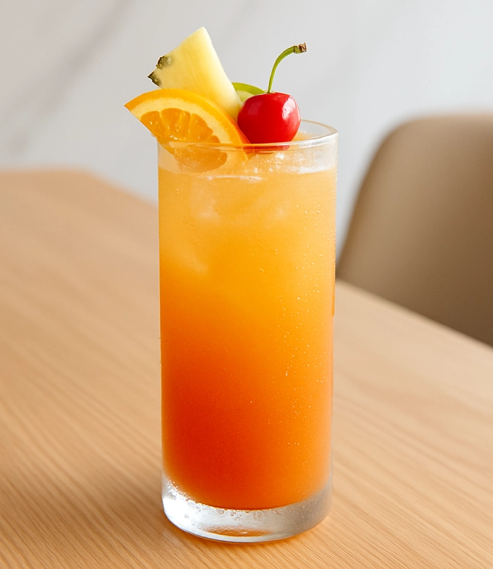 Tropical fruit juice cocktail served in a chilled glass with orange, pineapple, and cherry garnish.