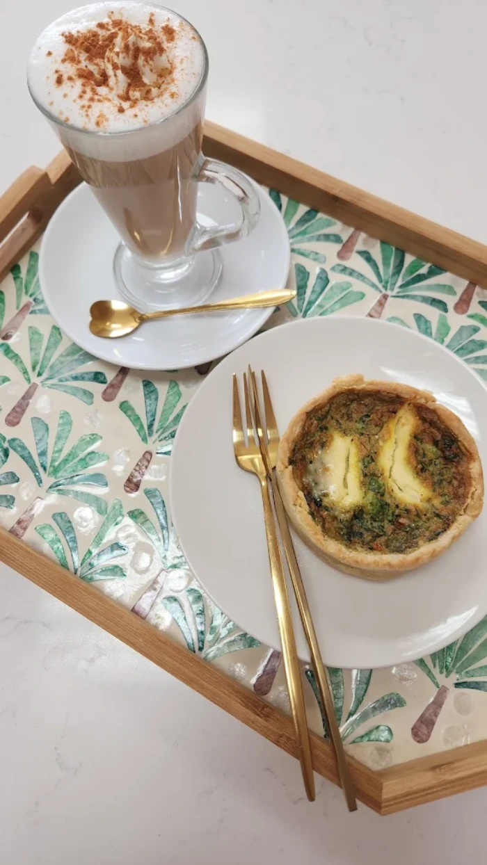Latte with cinnamon and a savory quiche on a tray.