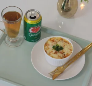 Plato individual de comida horneada acompañado de una bebida de guaraná y una infusión caliente.