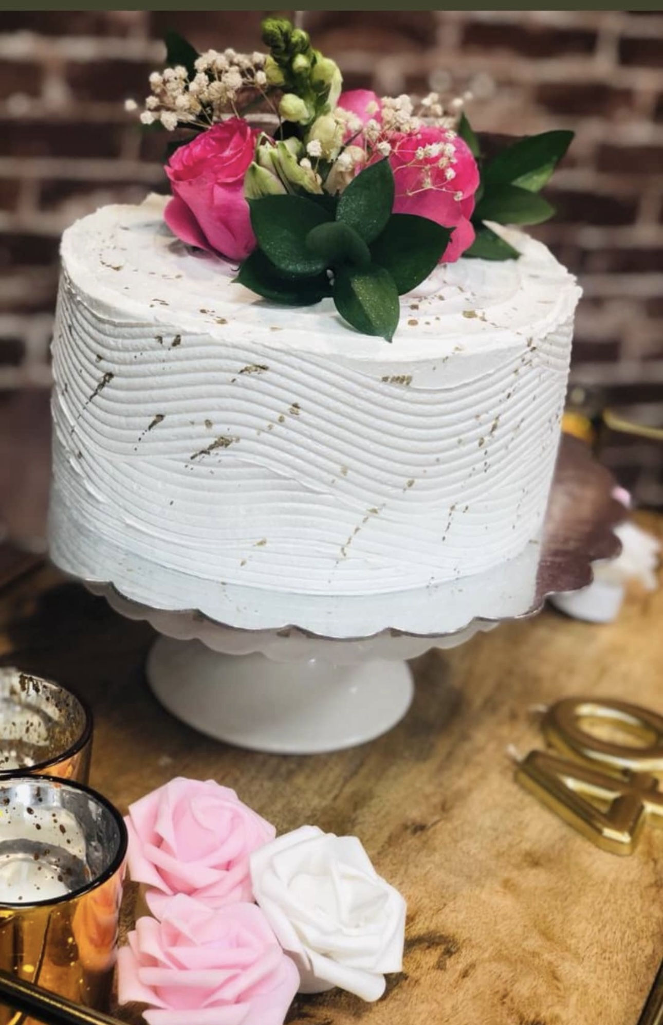 Elegant white cake with textured frosting and fresh pink roses on top.