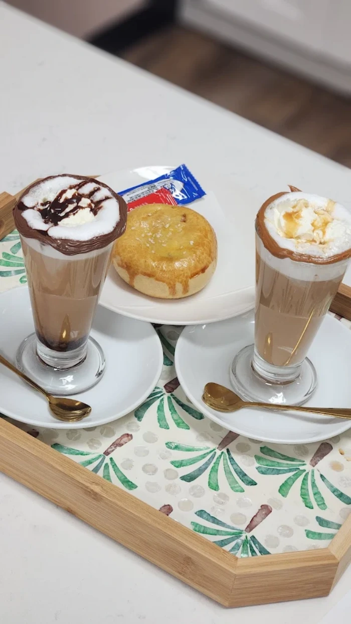 Bandeja con dos cafés latte decorados con crema y chocolate, acompañados de un pan dulce y cubiertos de chocolate.